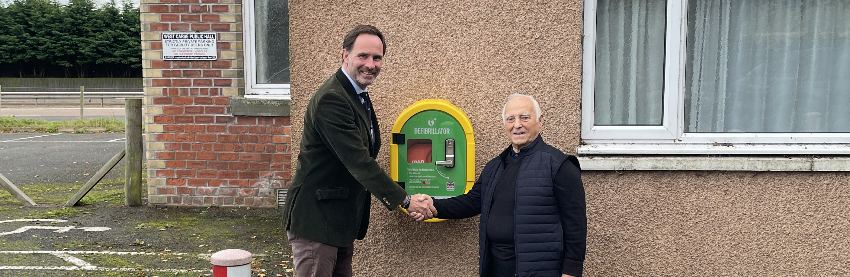 Two men shake hands in front of Public Access Defibrillator