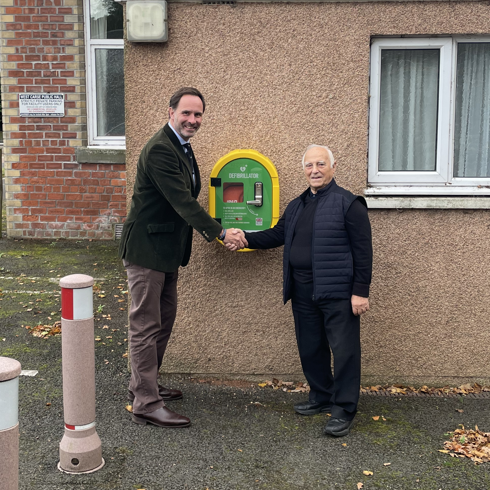 Two men shake hands in front of Public Access Defibrillator