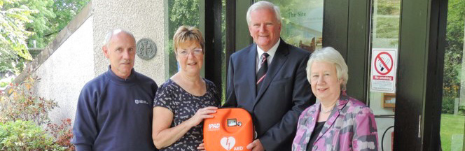 Four people pose with a defibrillator
