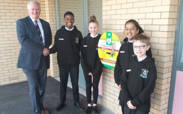 A man and four children pose next to a Public Access Defibrillator