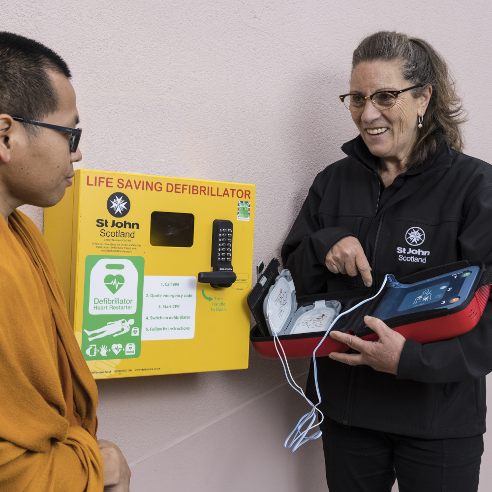 A St John Scotland volunteer demonstrates a defibrillator to a man