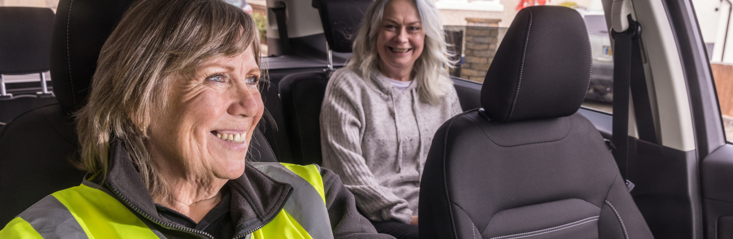 A woman in hi vis drives a car with a passenger in the back seat
