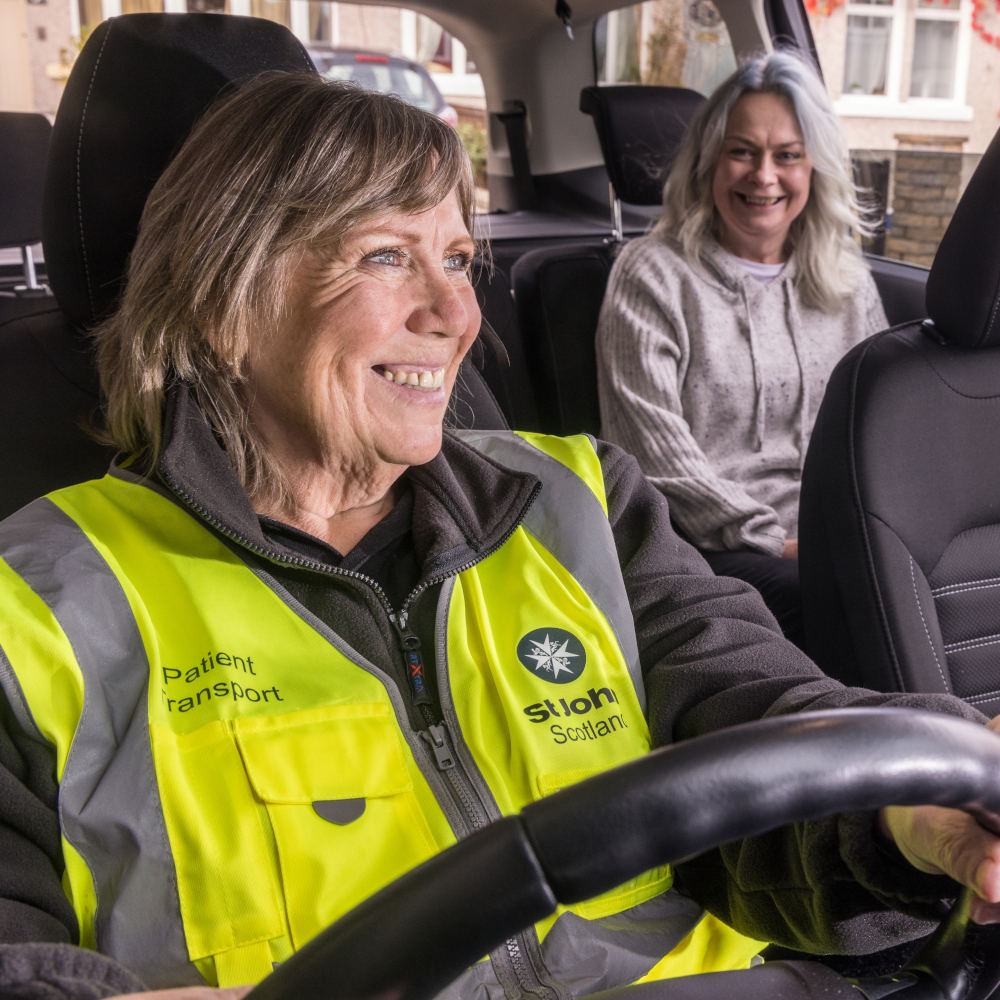 A woman in hi vis drives a car with a passenger in the back seat