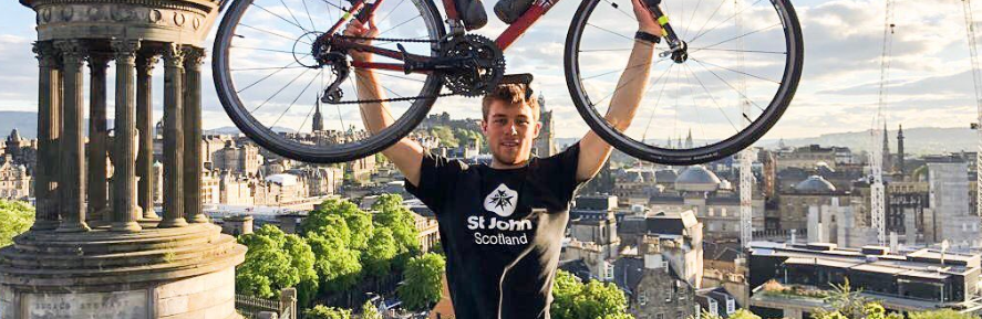 A man in a St John Scotland T shirt holds a bike above his head