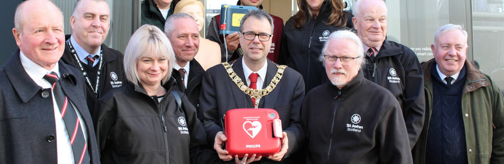A group of people pose with a defibrillator in front of a tram