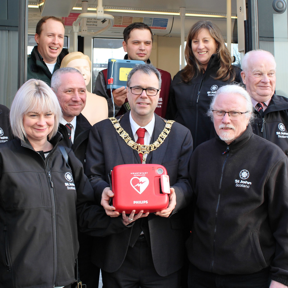 A group of people pose with a defibrillator in front of a tram
