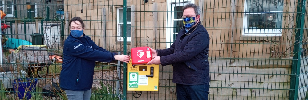 Two people stand next to a public access defibrillator