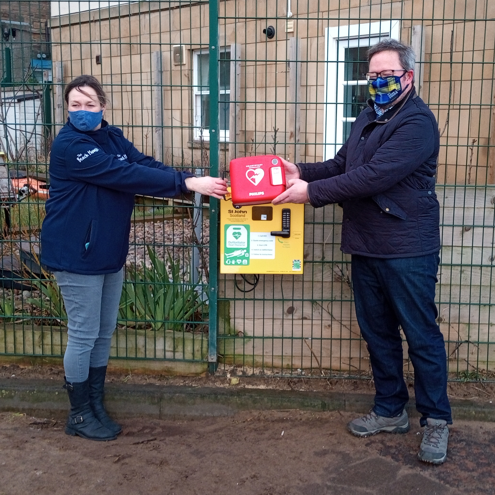 Two people stand next to a public access defibrillator