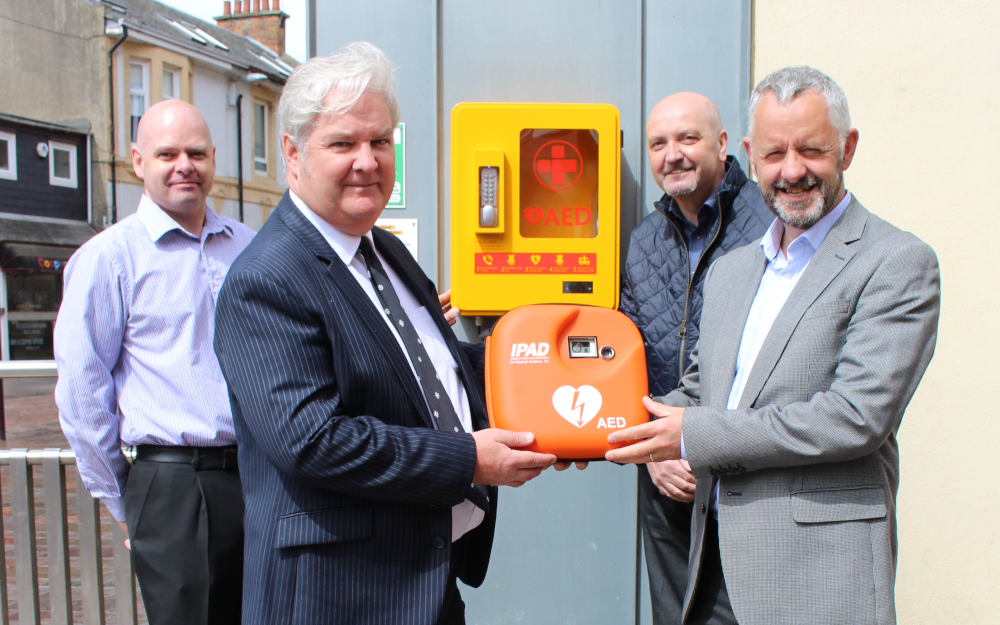 Four men pose with a defibrillator