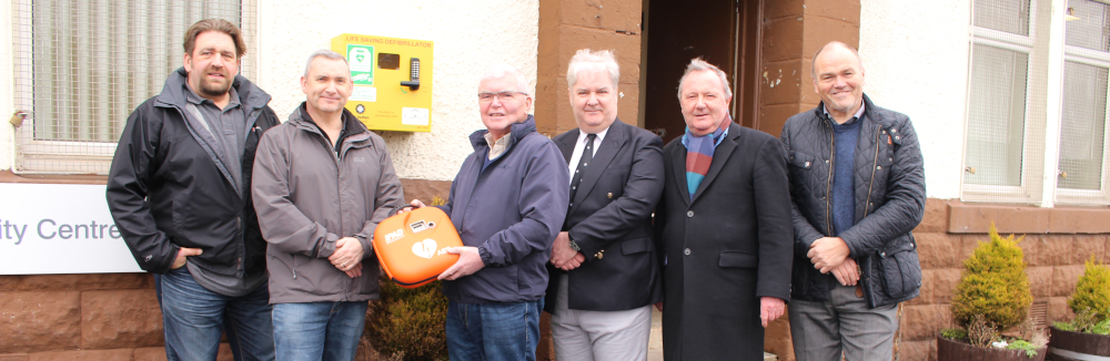A group of men pose with a defibrillator