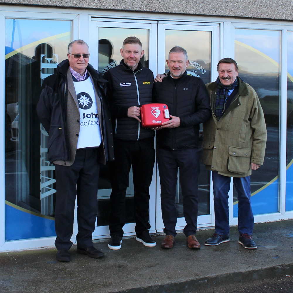 Four men pose with a defibrillator
