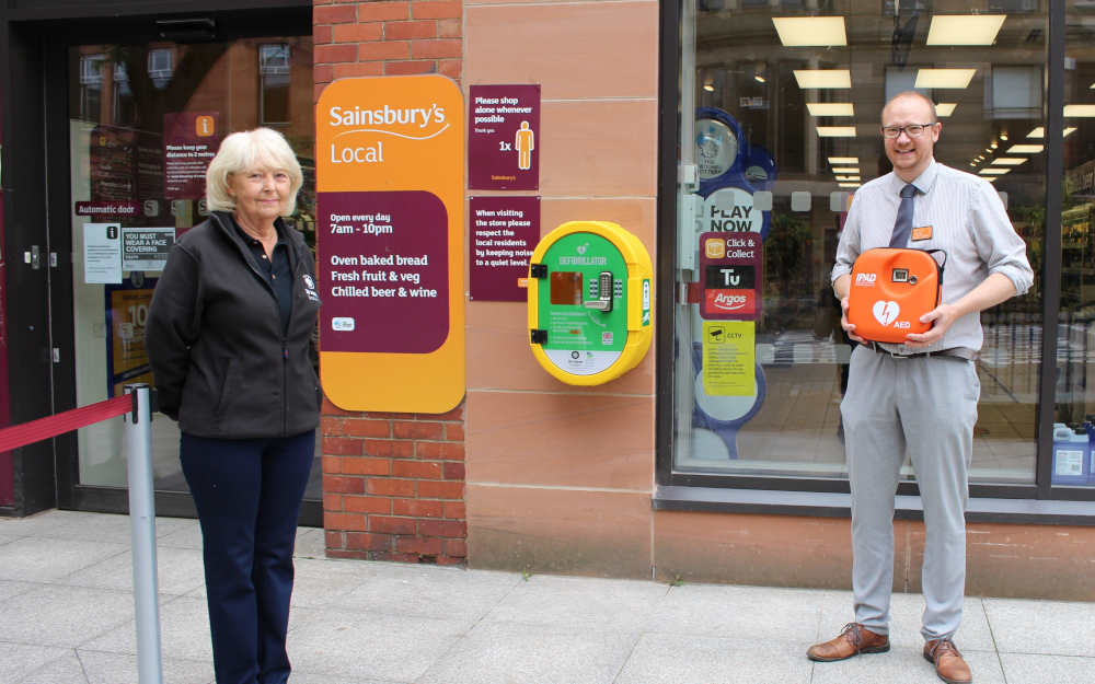 Two people stand next to a public access defibrillator
