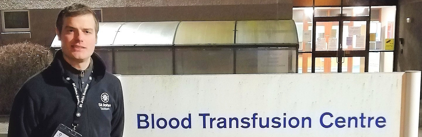 A St John Scotland volunteer stands next to a sign saying Blood Transfusion Centre