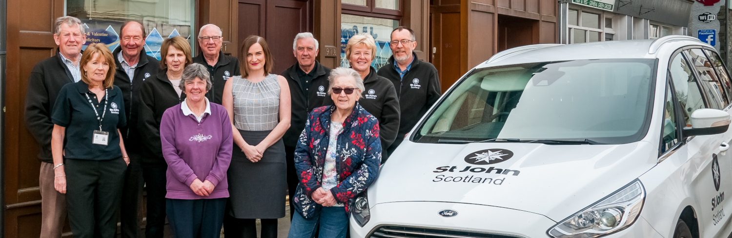 A group of people pose next to a St John Scotland car