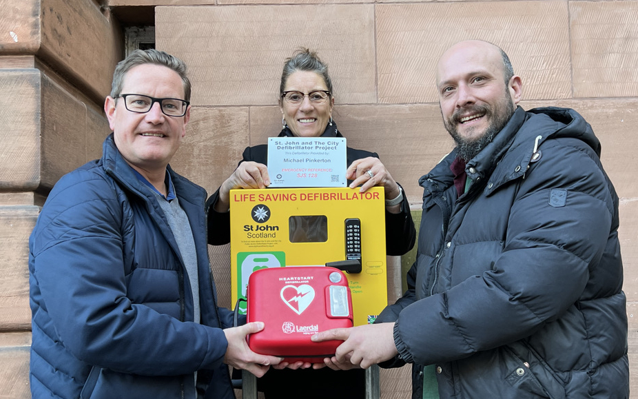 Three people pose with a defibrillator