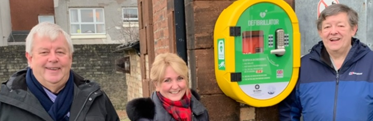 Three people pose with a defibrillator