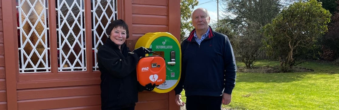 A woman and man pose next to a defibrillator