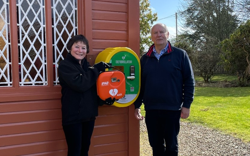 A woman and man pose next to a defibrillator