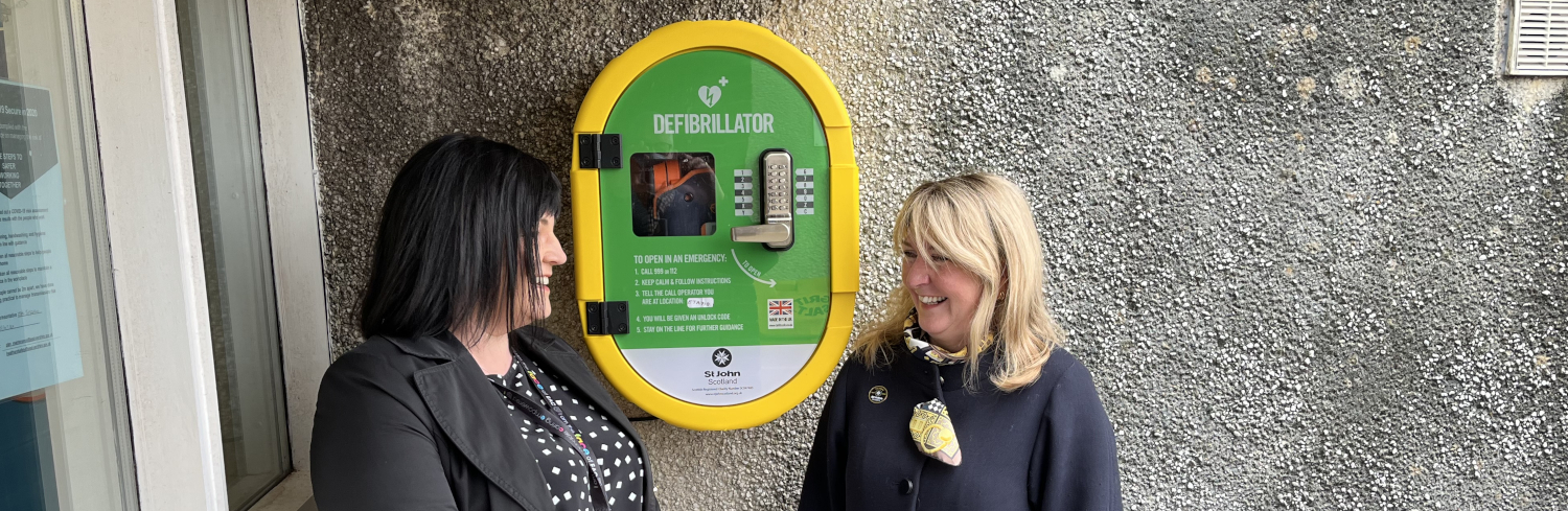 Two women stand next to a Public Access Defibrillator