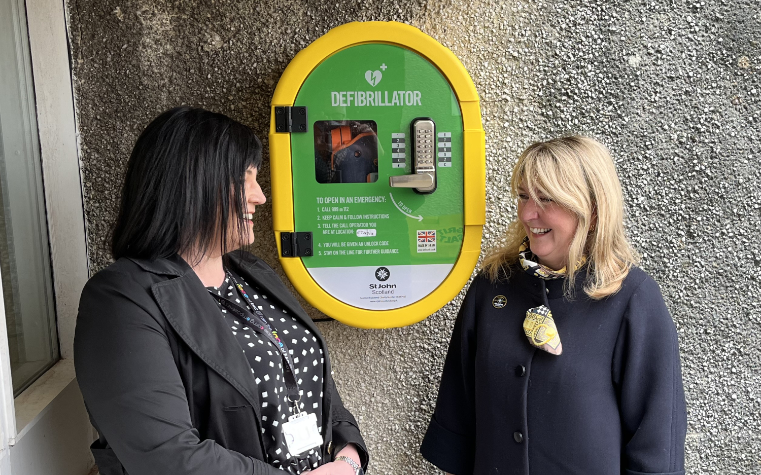 Two women stand next to a Public Access Defibrillator