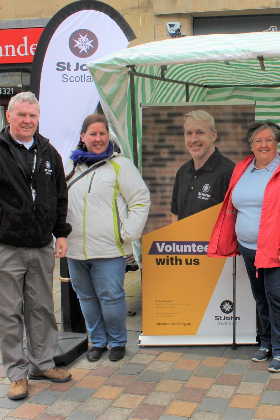 A group of three volunteers pose in front of a pop up banner and stand