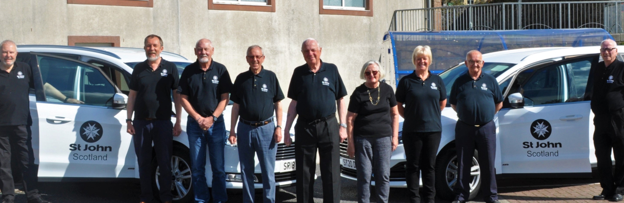 A group of St John Scotland volunteers with two cars
