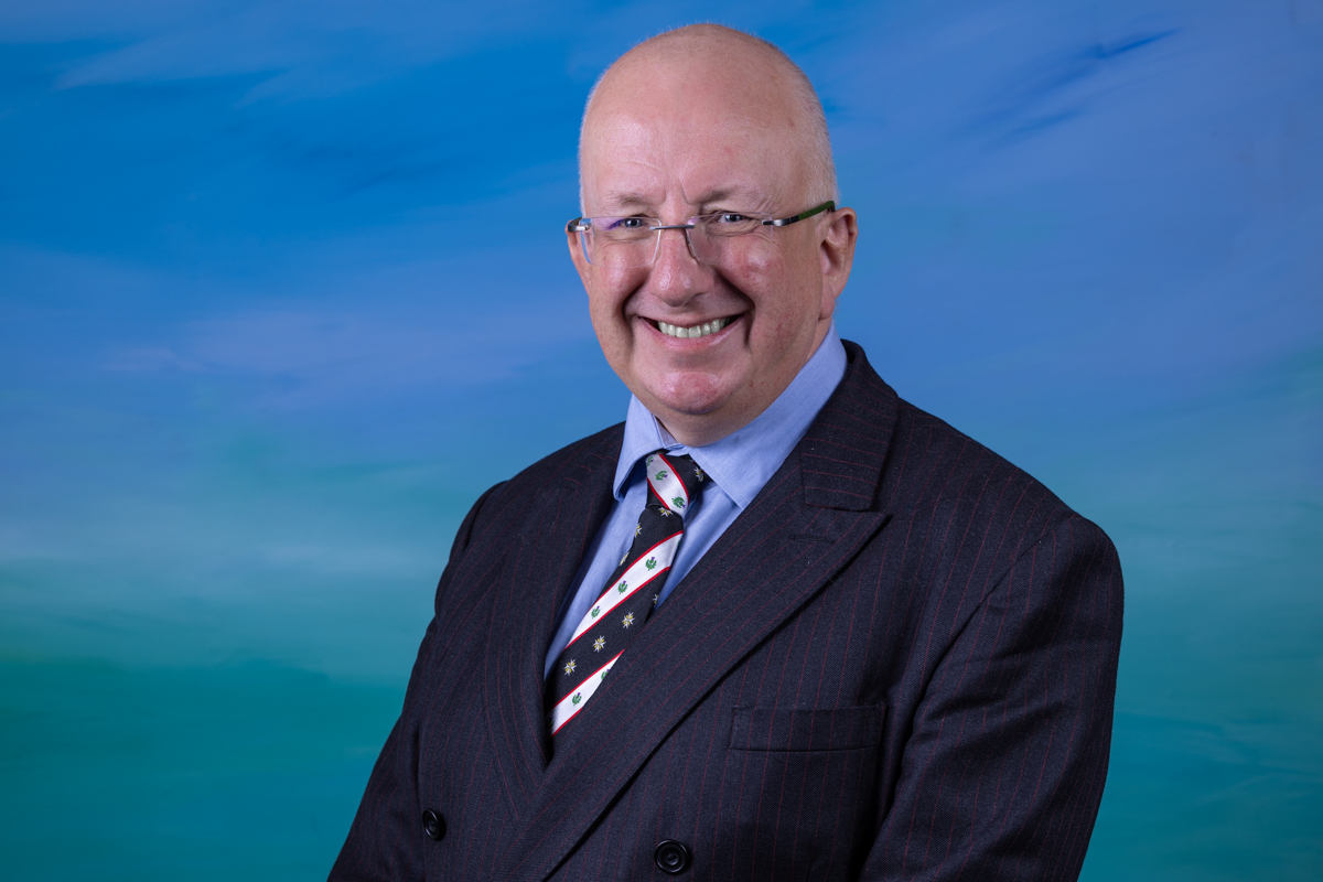 A man with glasses sits in front of a blue background