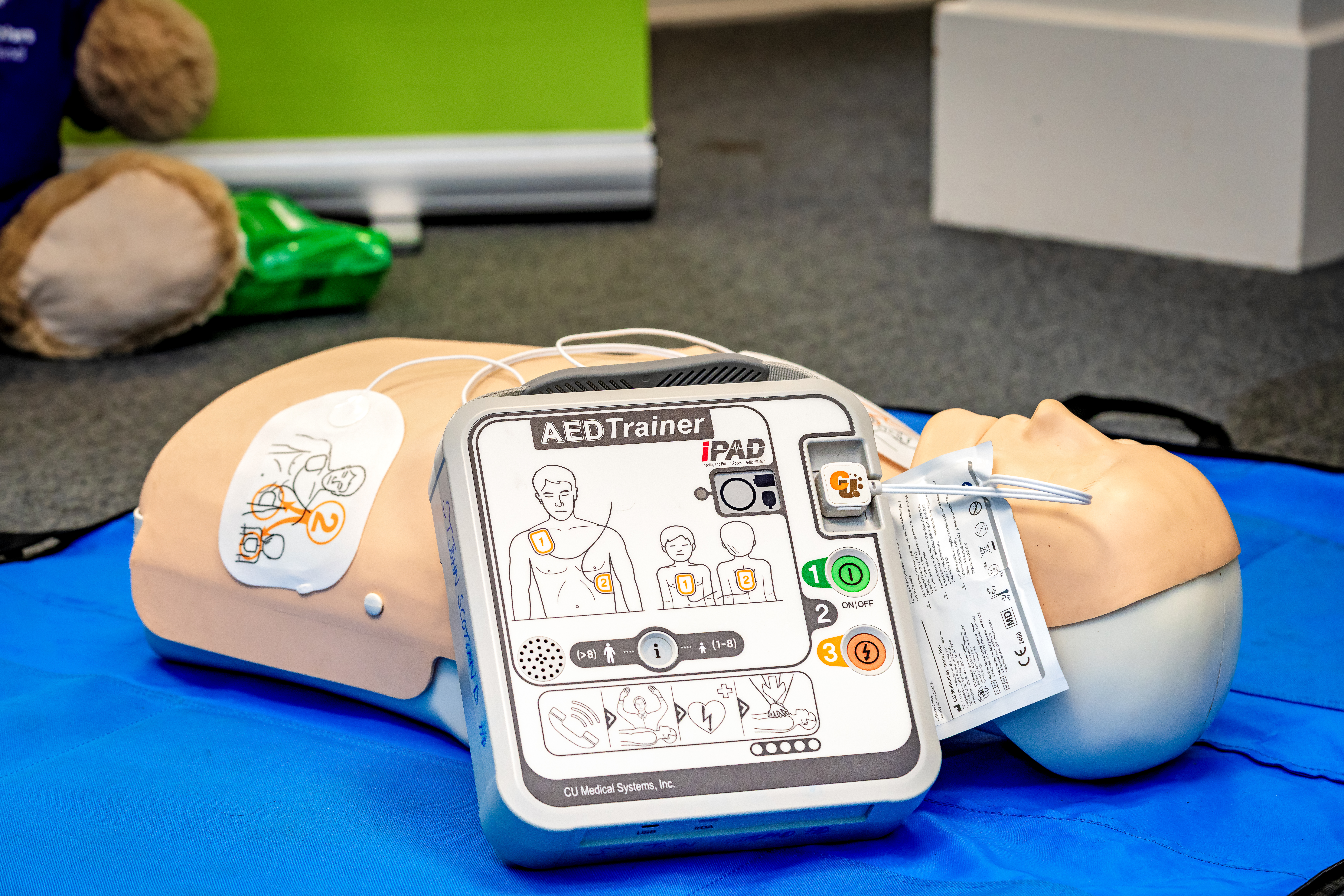 A close-up of a training defibrillator next to a dummy used in training
