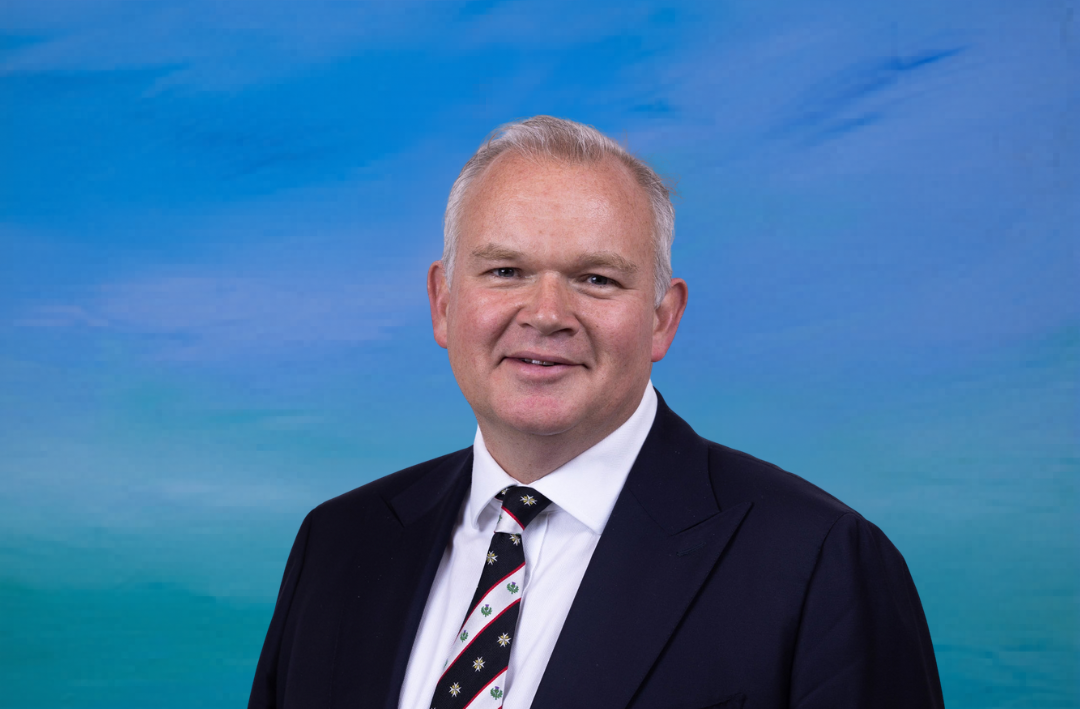 A man in a suit in front of a blue background, with a St John Scotland tie