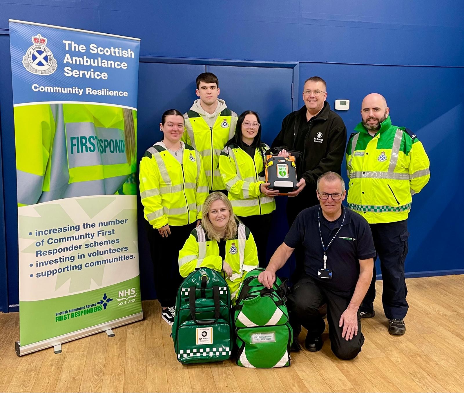 Seven people stand holding kit for Community First Responders. 5 are in high-vis jackets.