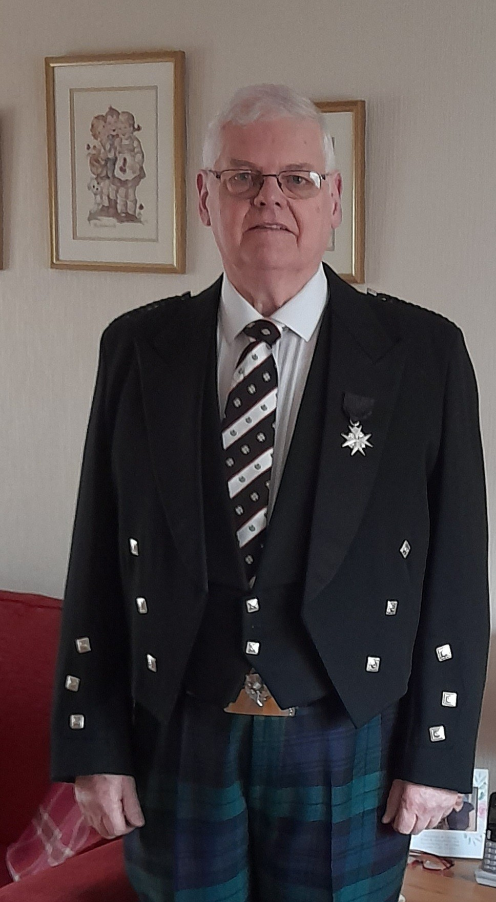 A man in tartan trousers and a black jacket, with a St John Scotland tie