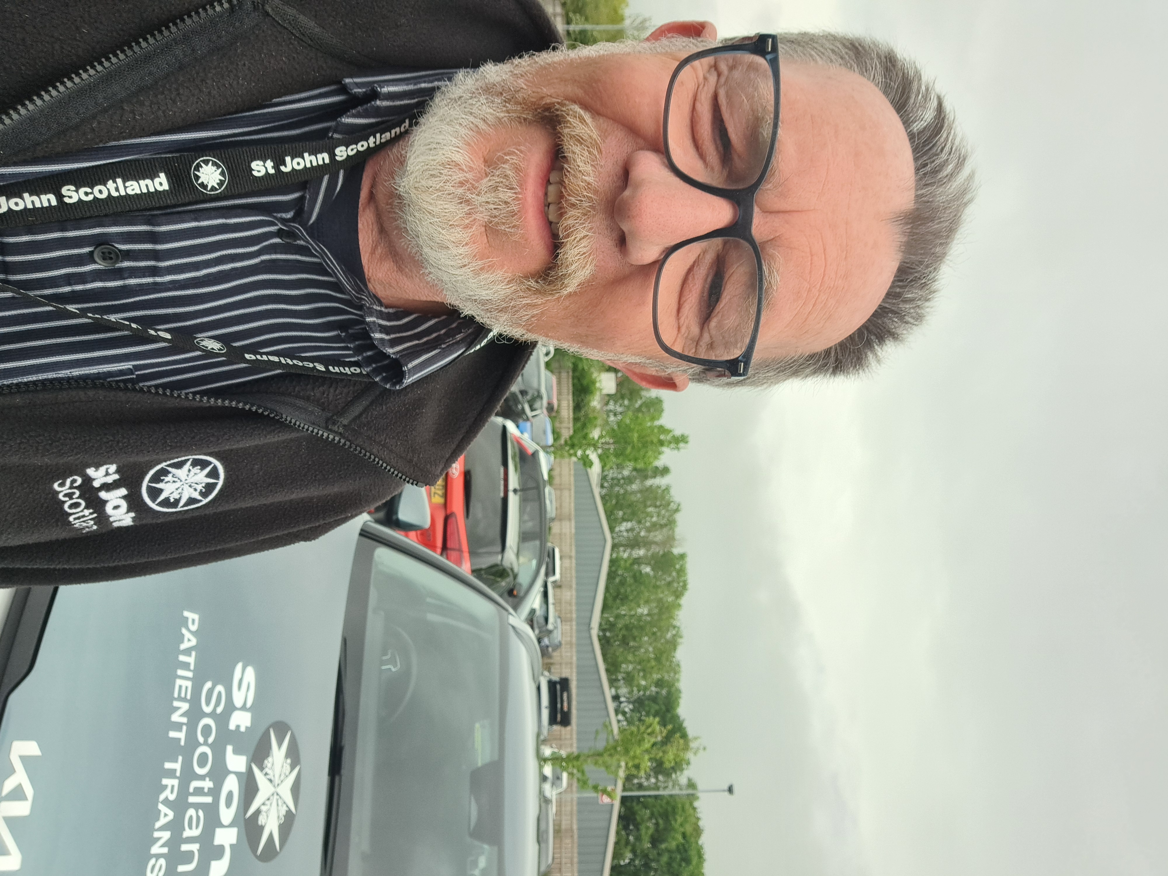 A man with a beard stands in front of a St John Scotland branded car