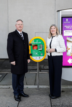 A man and woman standing outside the Scottish Parliament building beside a defibrillator